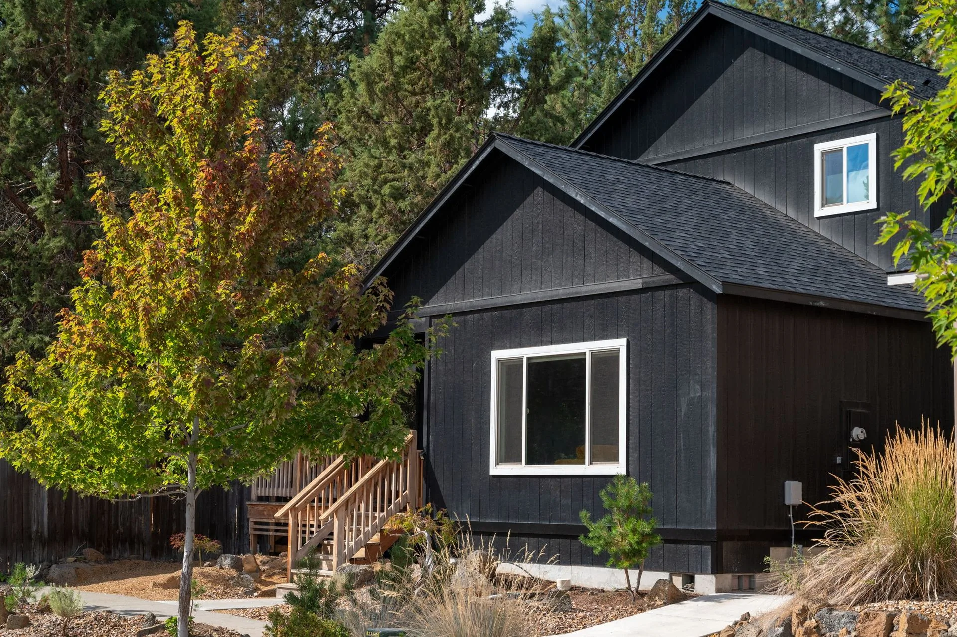 Dark-sided home with white window trim, a wooden entry stair, and leafy trees